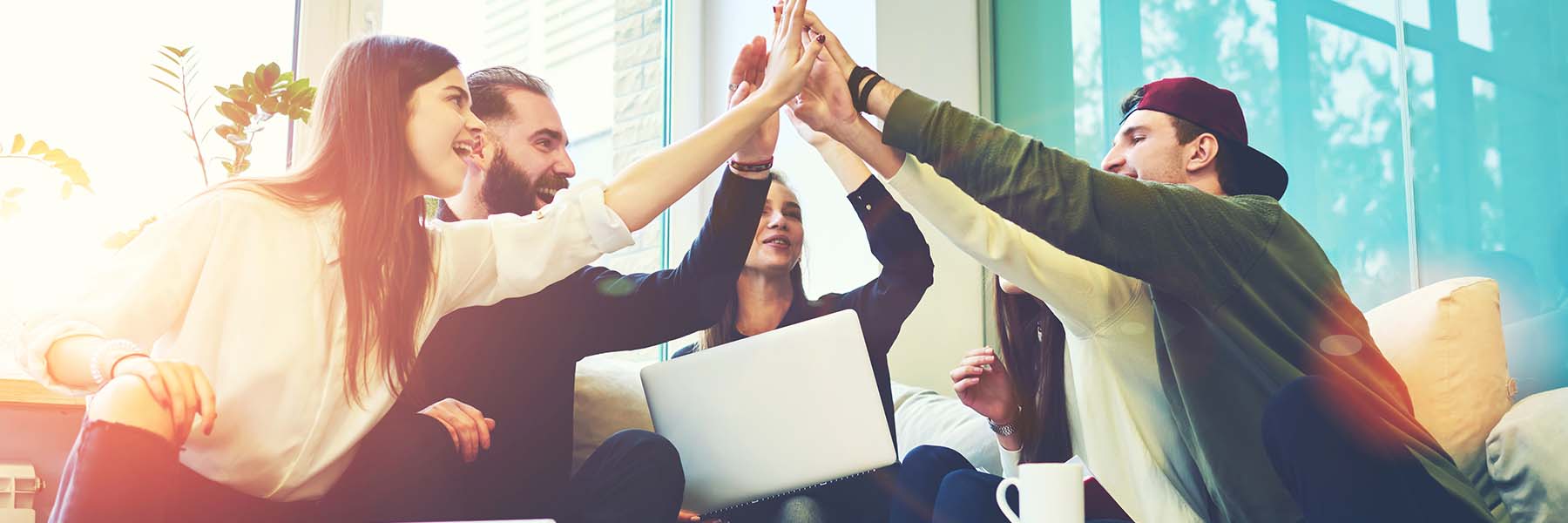 Gruppe von Menschen geben sich ein gemaischaftliche High Five über einem Laptop